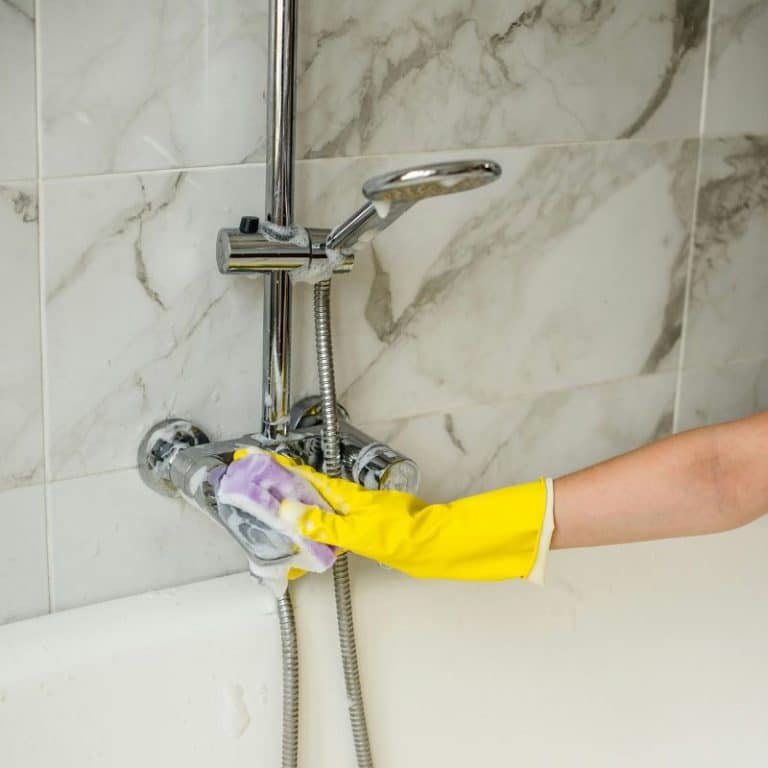 gloved hand cleaning a shower faucet