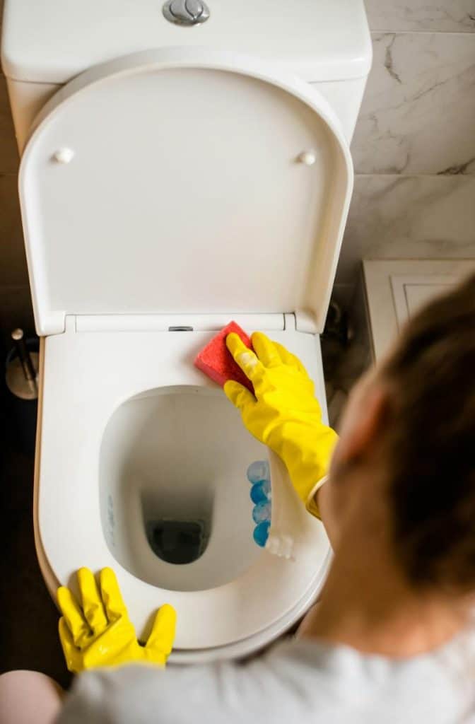 woman cleaning a toilet while wearing cleaning gloves