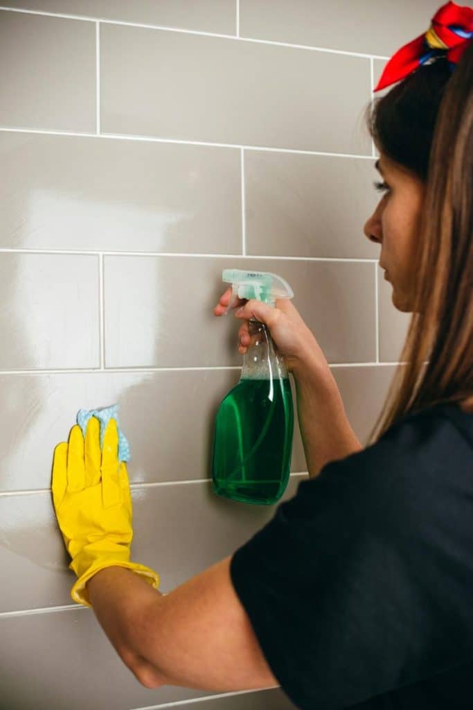 woman wearing cleaning glove cleaning a shower wall